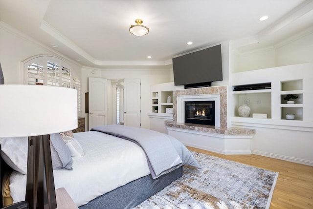 bedroom featuring ornamental molding, a fireplace, light hardwood / wood-style floors, and a tray ceiling