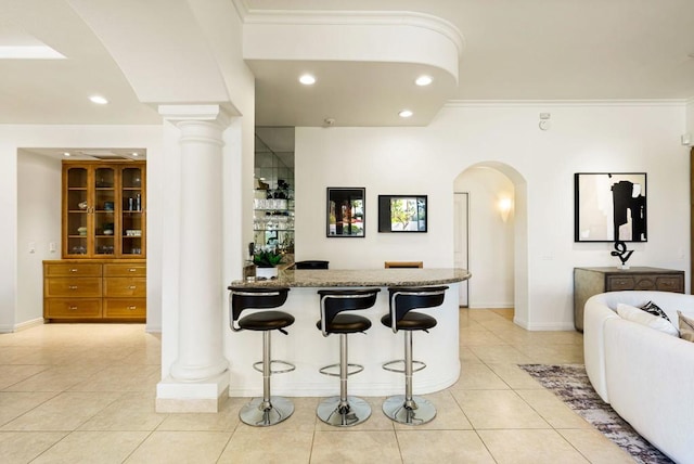 bar featuring light tile patterned flooring, crown molding, decorative columns, and stone counters