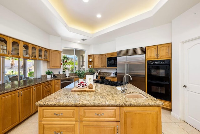 kitchen with sink, a center island with sink, light stone counters, and black appliances