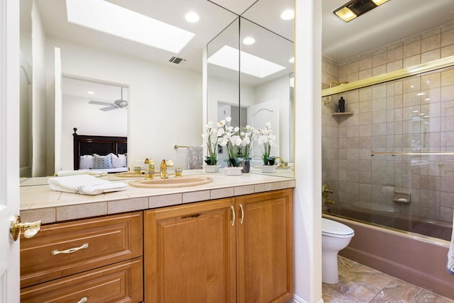 full bathroom featuring toilet, combined bath / shower with glass door, a skylight, vanity, and ceiling fan