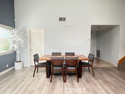 dining area with light wood-style floors, baseboards, visible vents, and a high ceiling