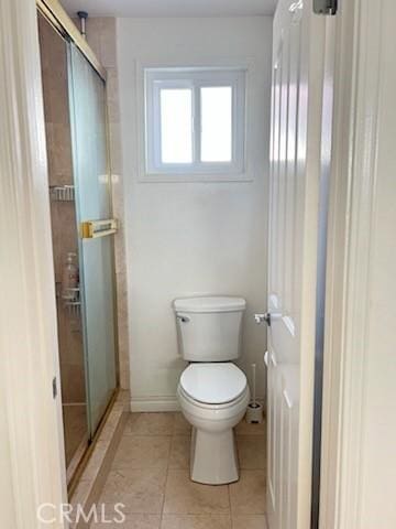 bathroom with a stall shower, baseboards, toilet, and tile patterned floors