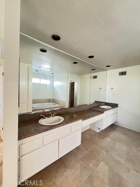 full bathroom featuring a sink, visible vents, a bath, and double vanity