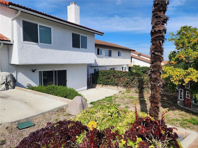 back of house with a tile roof, a patio, a chimney, and stucco siding