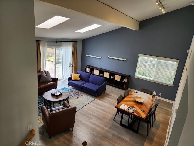 living room with lofted ceiling with skylight, track lighting, wood finished floors, and baseboards