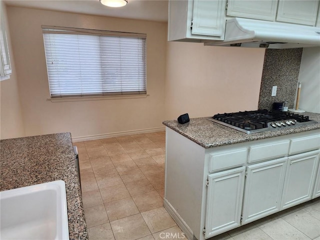 kitchen with stainless steel gas cooktop, under cabinet range hood, baseboards, backsplash, and a sink