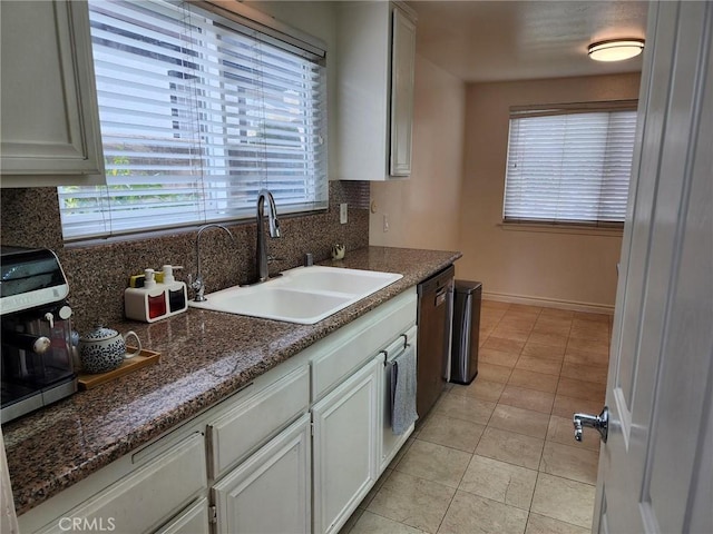 kitchen with light tile patterned floors, backsplash, a sink, dishwasher, and baseboards