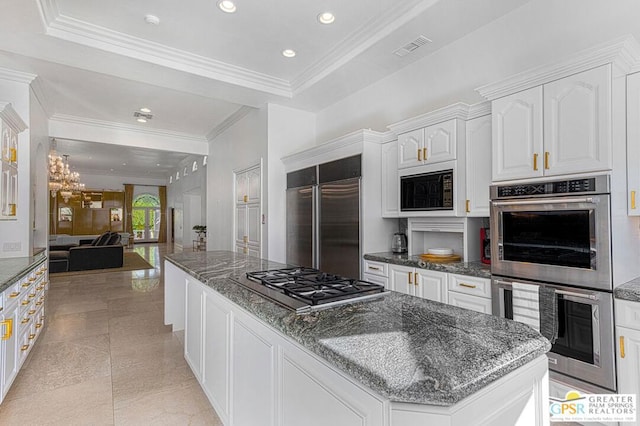 kitchen featuring white cabinetry, built in appliances, dark stone countertops, a raised ceiling, and a kitchen island