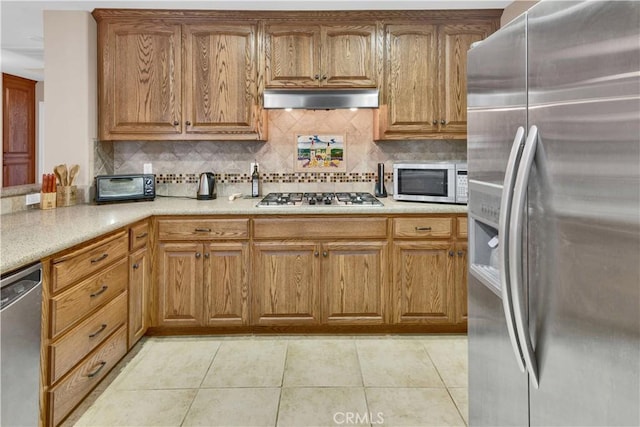 kitchen featuring light tile patterned floors, stainless steel appliances, exhaust hood, light countertops, and brown cabinets