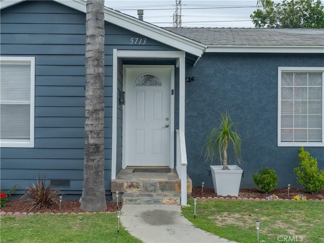 doorway to property with roof with shingles and stucco siding