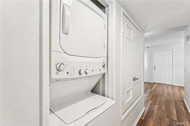 washroom with hardwood / wood-style flooring and stacked washer / drying machine