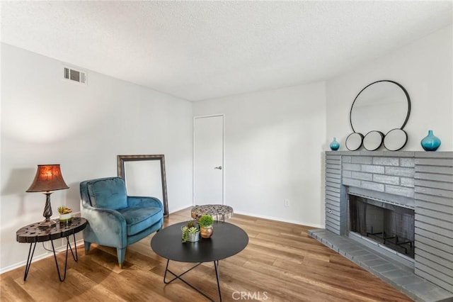 sitting room with a brick fireplace, hardwood / wood-style floors, and a textured ceiling