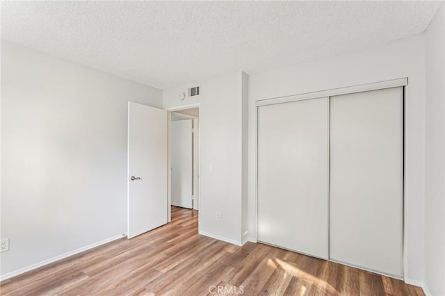 unfurnished bedroom with a textured ceiling, light hardwood / wood-style floors, and a closet