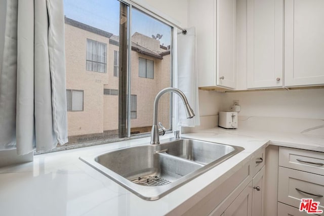 kitchen with white cabinetry, sink, and light stone countertops