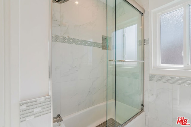 bathroom with plenty of natural light, tile walls, and shower / bath combination with glass door