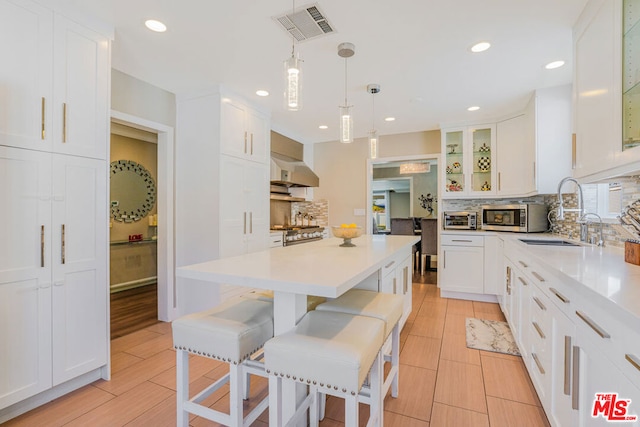 kitchen with a breakfast bar, sink, white cabinetry, pendant lighting, and backsplash