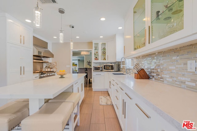 kitchen with decorative light fixtures, sink, white cabinets, a kitchen bar, and wall chimney range hood