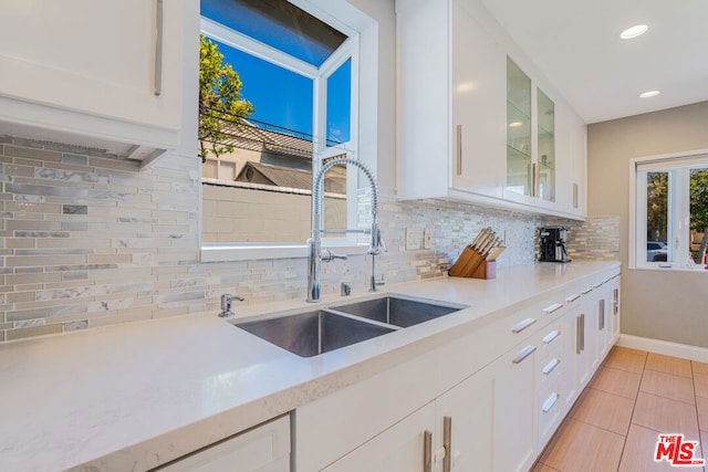 kitchen featuring sink, backsplash, light tile patterned floors, and white cabinets