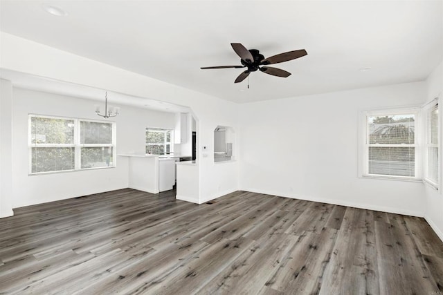 unfurnished living room with ceiling fan with notable chandelier and dark wood-type flooring