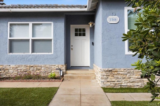 view of exterior entry featuring a tile roof, stone siding, and stucco siding