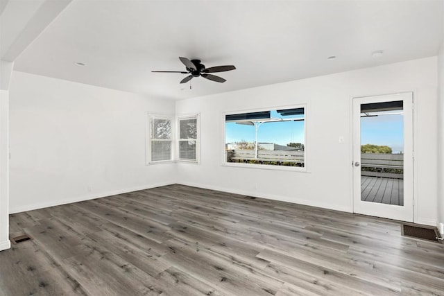 empty room featuring ceiling fan, visible vents, baseboards, and wood finished floors