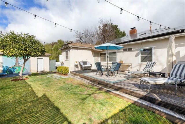 rear view of house featuring a lawn, a deck, a shed, and solar panels