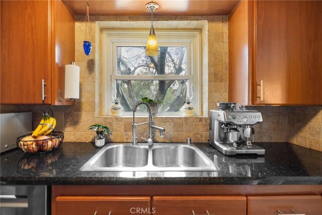 kitchen featuring dark stone counters, decorative light fixtures, sink, and backsplash