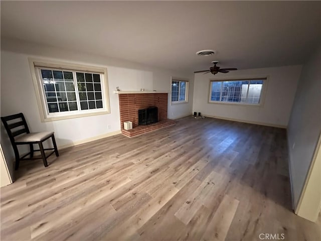 unfurnished living room with baseboards, visible vents, a ceiling fan, wood finished floors, and a brick fireplace