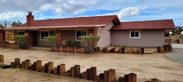 back of property featuring stucco siding, a chimney, roof with shingles, and fence