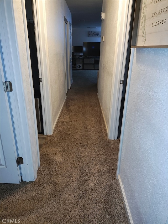 corridor with dark colored carpet, a textured wall, and baseboards