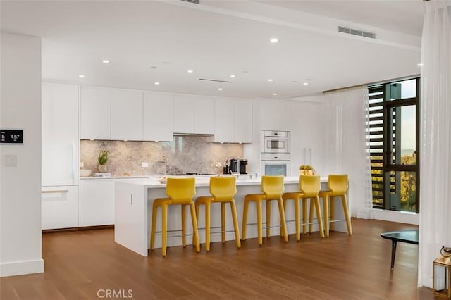 kitchen featuring a kitchen island with sink, backsplash, a breakfast bar, and white cabinets