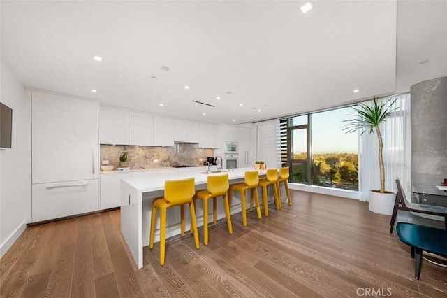 kitchen with wood finished floors, modern cabinets, a center island with sink, and white cabinets