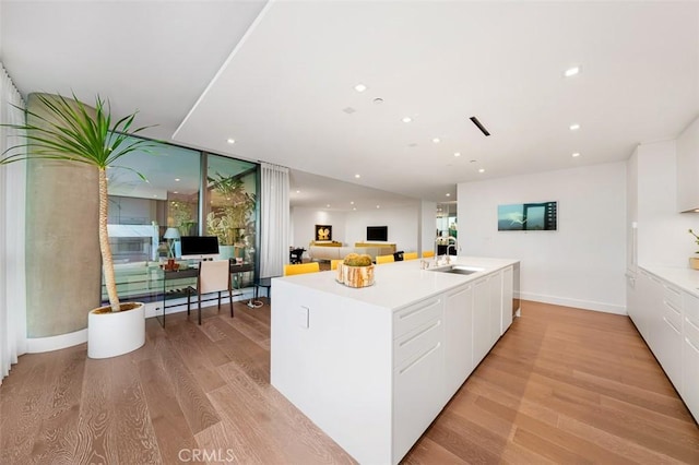 kitchen with white cabinetry, an island with sink, sink, and light wood-type flooring