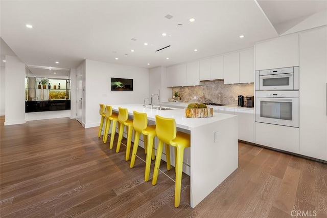 kitchen with a breakfast bar, white cabinetry, sink, white double oven, and a kitchen island with sink