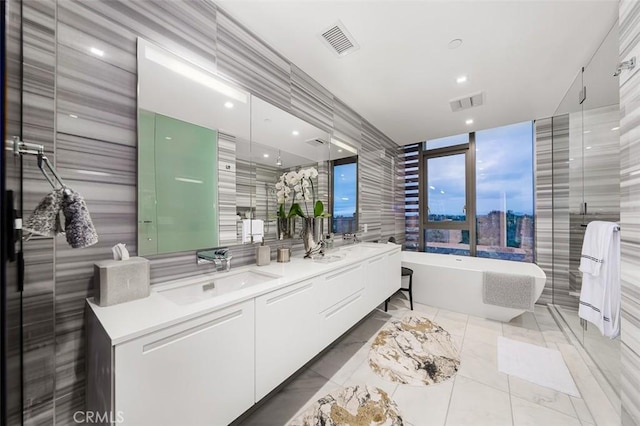 full bathroom with double vanity, a soaking tub, visible vents, and a sink