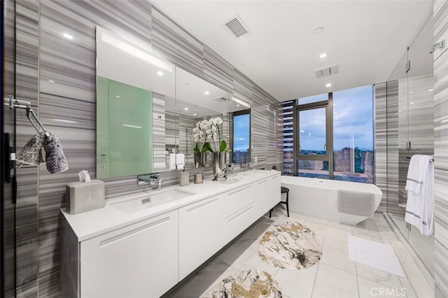 full bath with double vanity, marble finish floor, a sink, a soaking tub, and visible vents