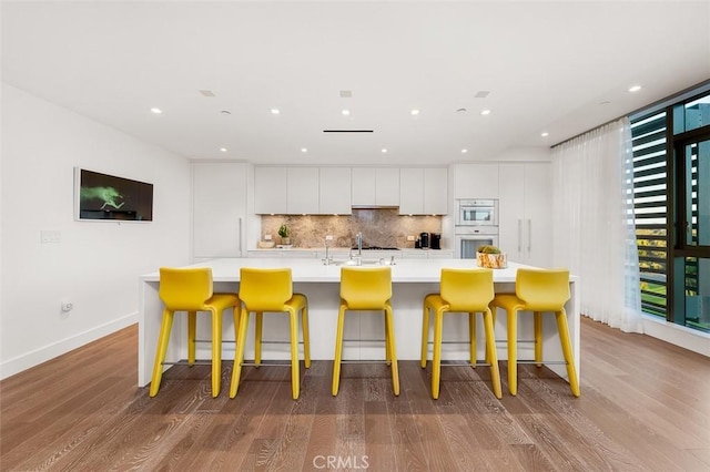 kitchen featuring wood finished floors, a large island, white cabinets, and backsplash