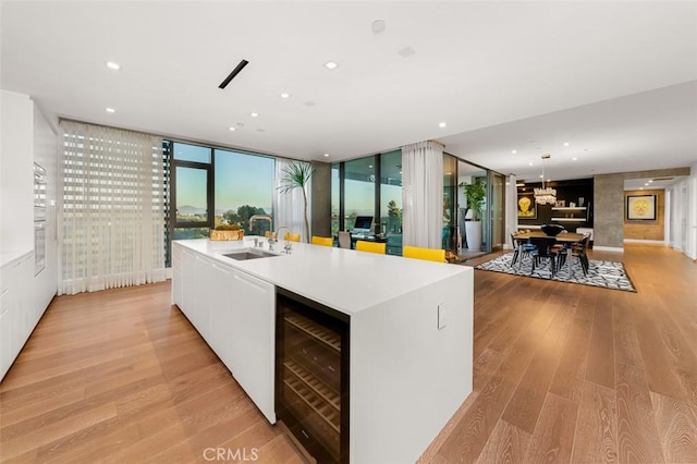 kitchen featuring a center island with sink, light wood-style flooring, a sink, wine cooler, and white cabinets