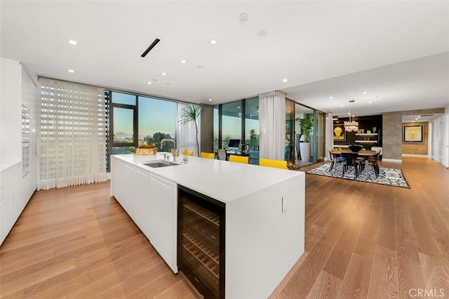 kitchen featuring a kitchen island with sink, beverage cooler, light wood-type flooring, and a sink