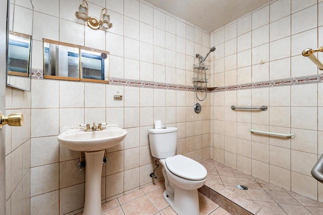 bathroom featuring tile patterned floors, toilet, sink, tile walls, and a tile shower