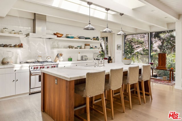 kitchen featuring stainless steel stove, hanging light fixtures, white cabinets, exhaust hood, and a large island with sink