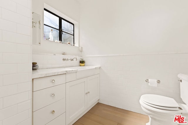 bathroom with hardwood / wood-style floors, vanity, tile walls, and toilet