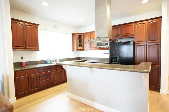 kitchen with black fridge with ice dispenser, light hardwood / wood-style flooring, a kitchen breakfast bar, and a center island