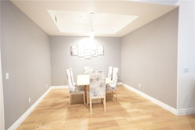 dining space featuring a raised ceiling and light wood-type flooring