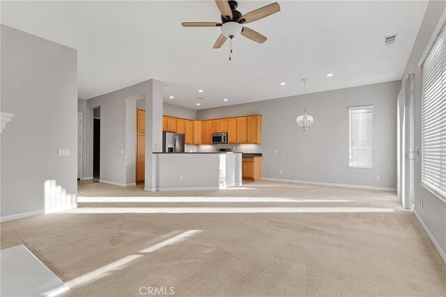 unfurnished living room featuring ceiling fan with notable chandelier and light colored carpet