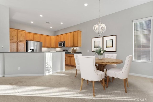 kitchen with a kitchen island, appliances with stainless steel finishes, pendant lighting, light colored carpet, and a notable chandelier