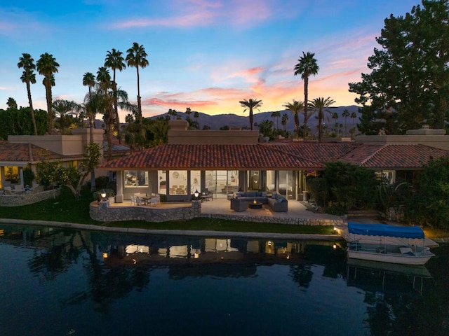 back house at dusk featuring an outdoor living space, a water and mountain view, and a patio area