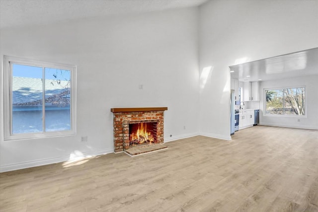 unfurnished living room with sink, light hardwood / wood-style floors, a brick fireplace, and a high ceiling