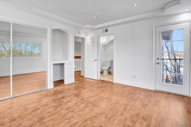 unfurnished bedroom with ensuite bathroom, access to exterior, a raised ceiling, and light hardwood / wood-style flooring