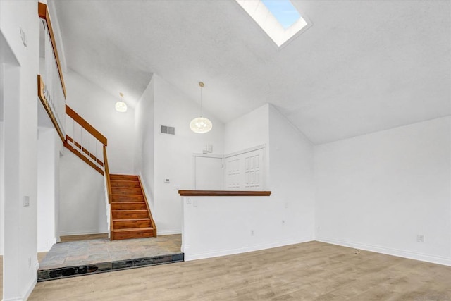 unfurnished living room with a skylight, high vaulted ceiling, and light wood-type flooring